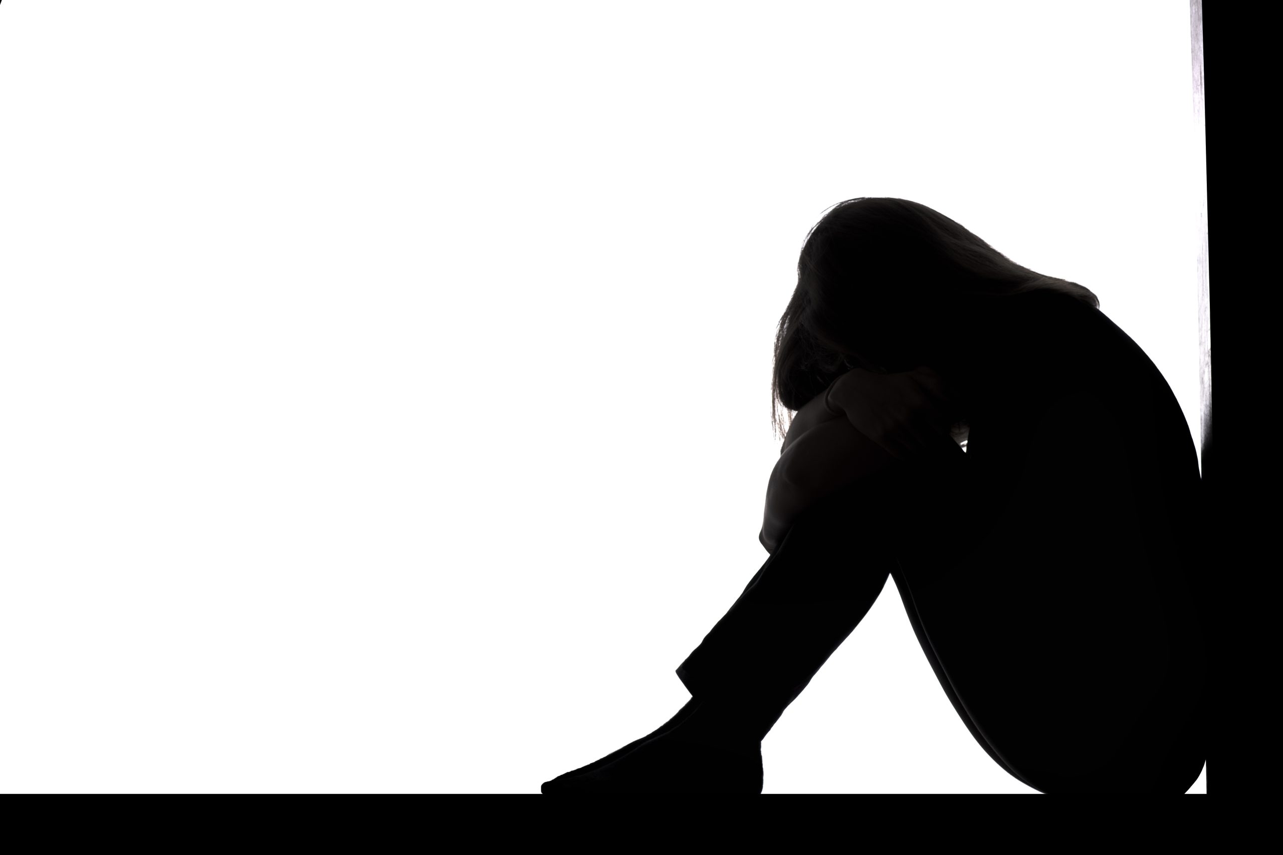 silhouette of a young woman sitting on the floor in a corner on a white isolated background, a sad girl crying putting head on knees,concept depression